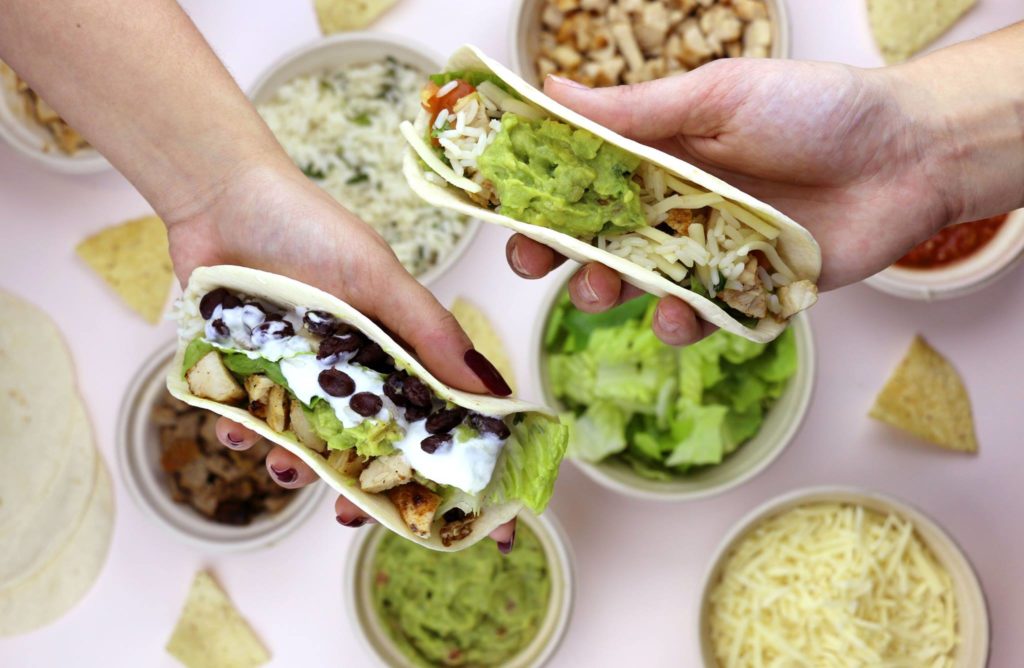Mucho Burrito Mexican food franchise Holding two tacos filled with Mucho burrito's fresh ingredients
